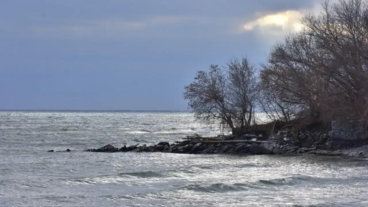 Calm Lake Ontario water lapping a rocky shoreline under a cloudy sky with sunlight breaking through.