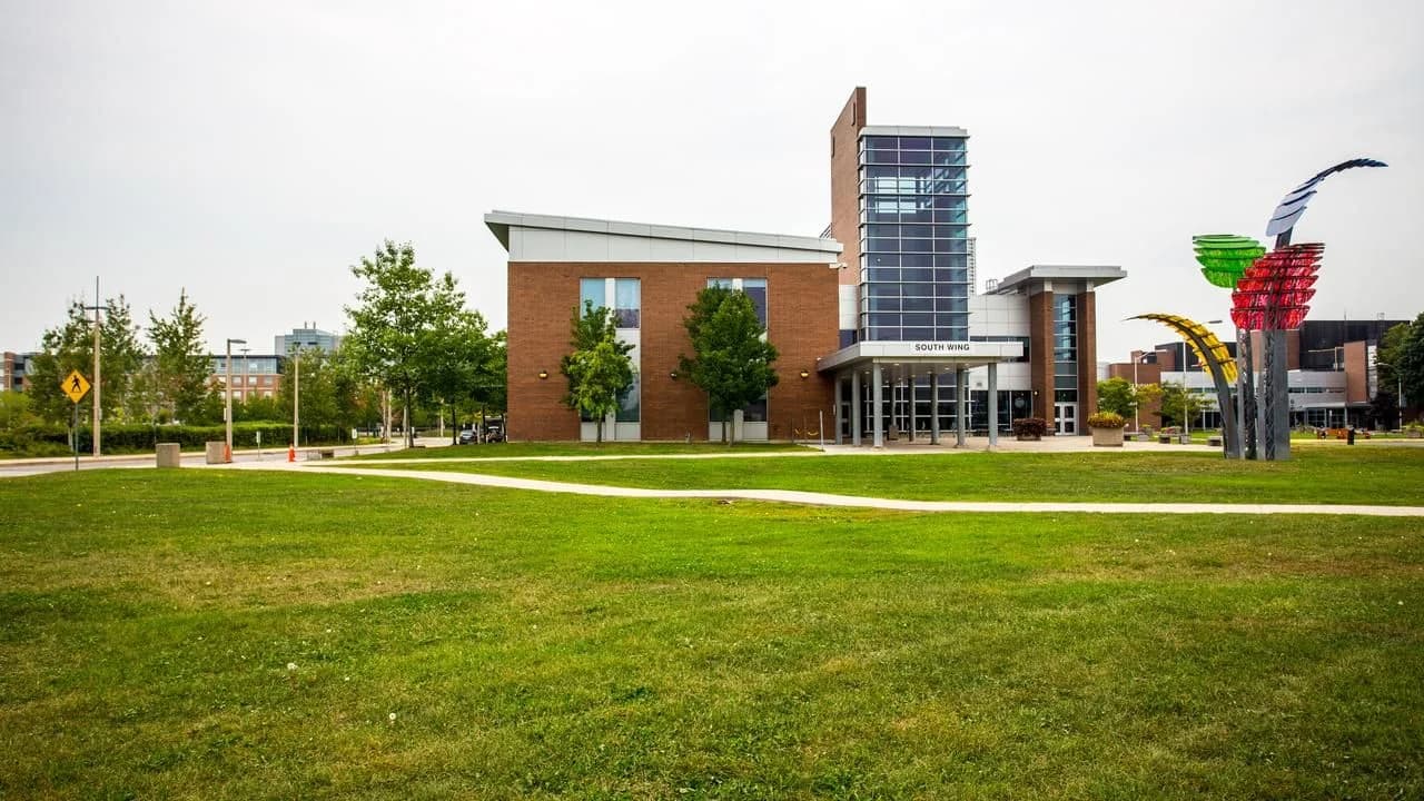 Durham College South Wing campus building in Oshawa with entrance plaza, lawn and sculptures; no people present