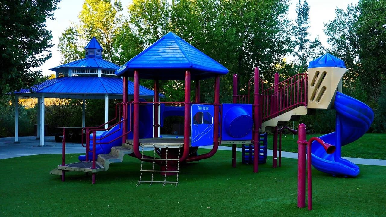 Colorful playground equipment — slides and towers — in a park, empty of people. Illustrative image, not Ashgrove Park.